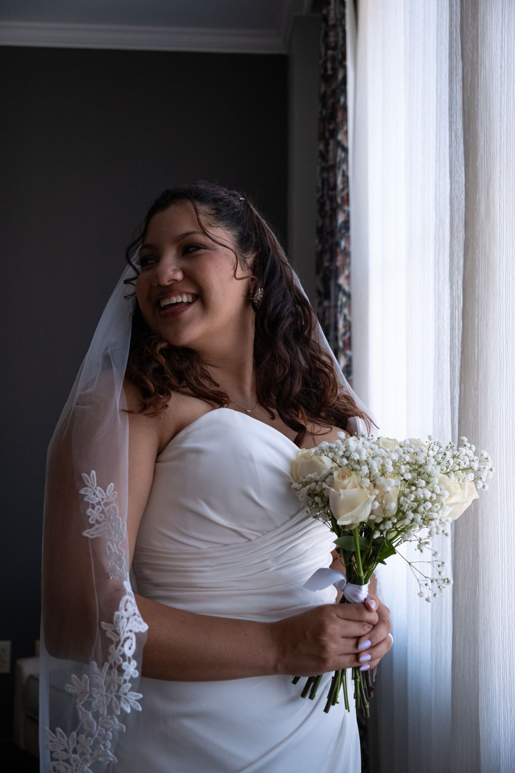 Bride in a veil holding a bouquet by a bright window