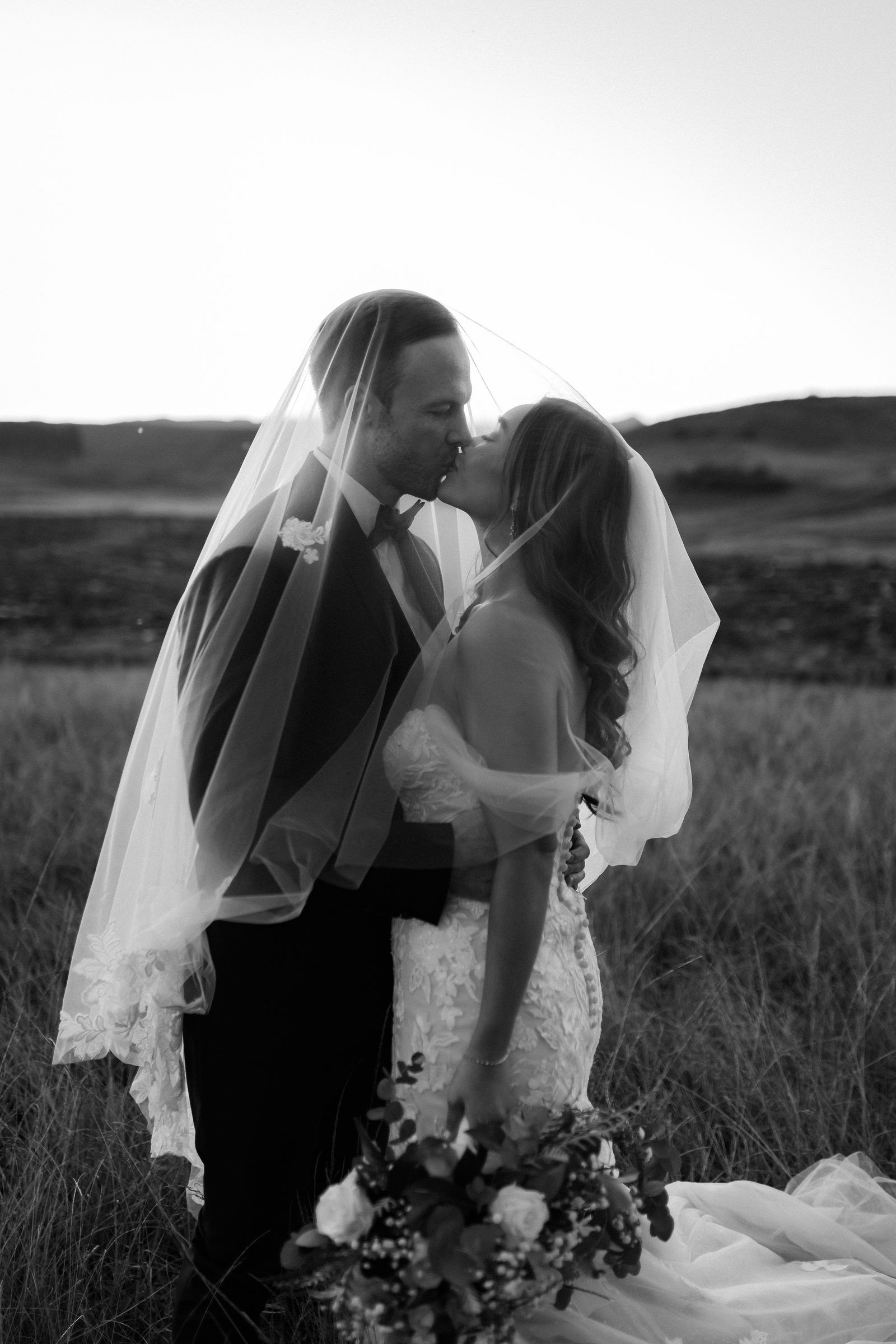 Black and white photo of a couple kissing beneath the veil