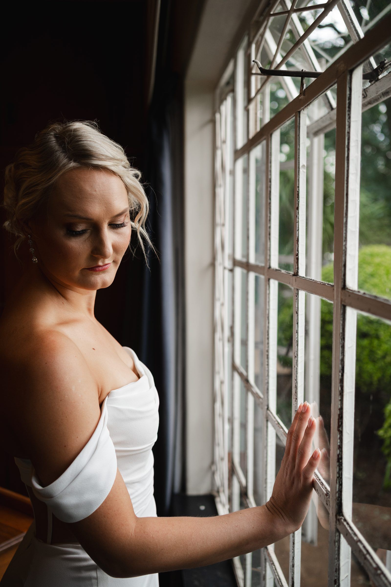 Bride in an off-shoulder gown beside tall windows